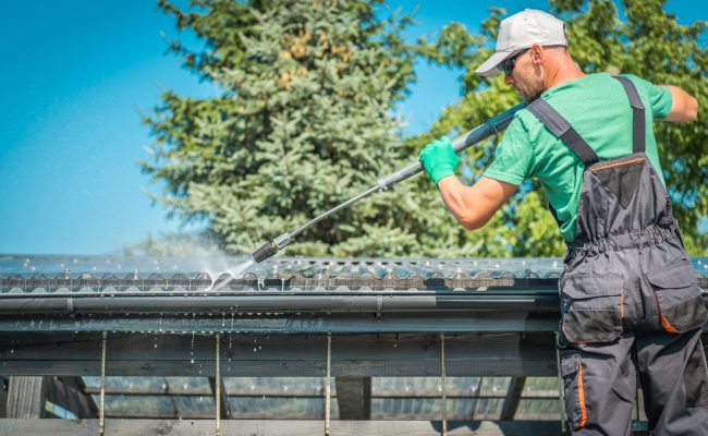 Roof and Gutters Power Cleaning Using Pressure Washer. Caucasian Worker.